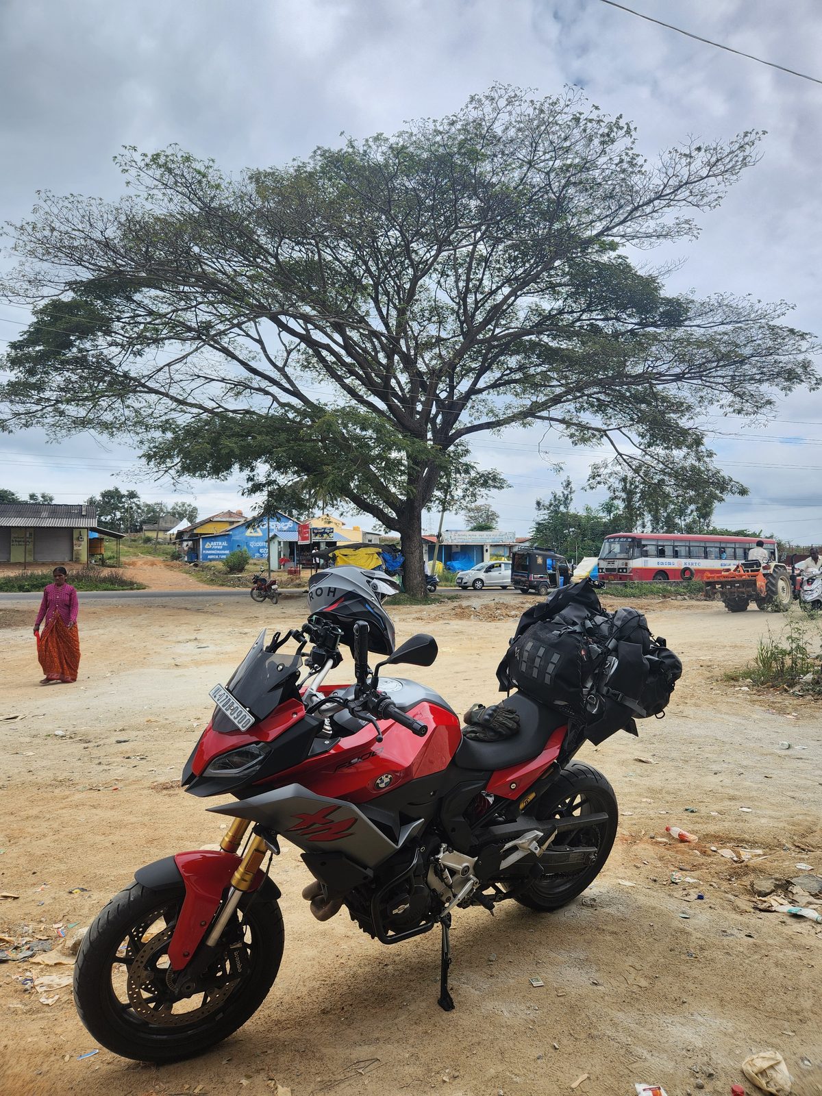 The motorcycle parked beside a large tree on the road to Chikkamagaluru under a cloudy sky