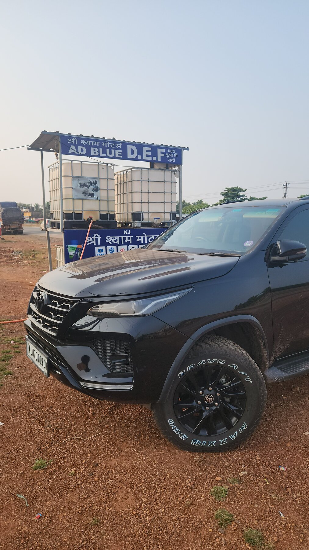 The Toyota Fortuner parked outside a small roadside AdBlue refill station with blue and white IBC tanks