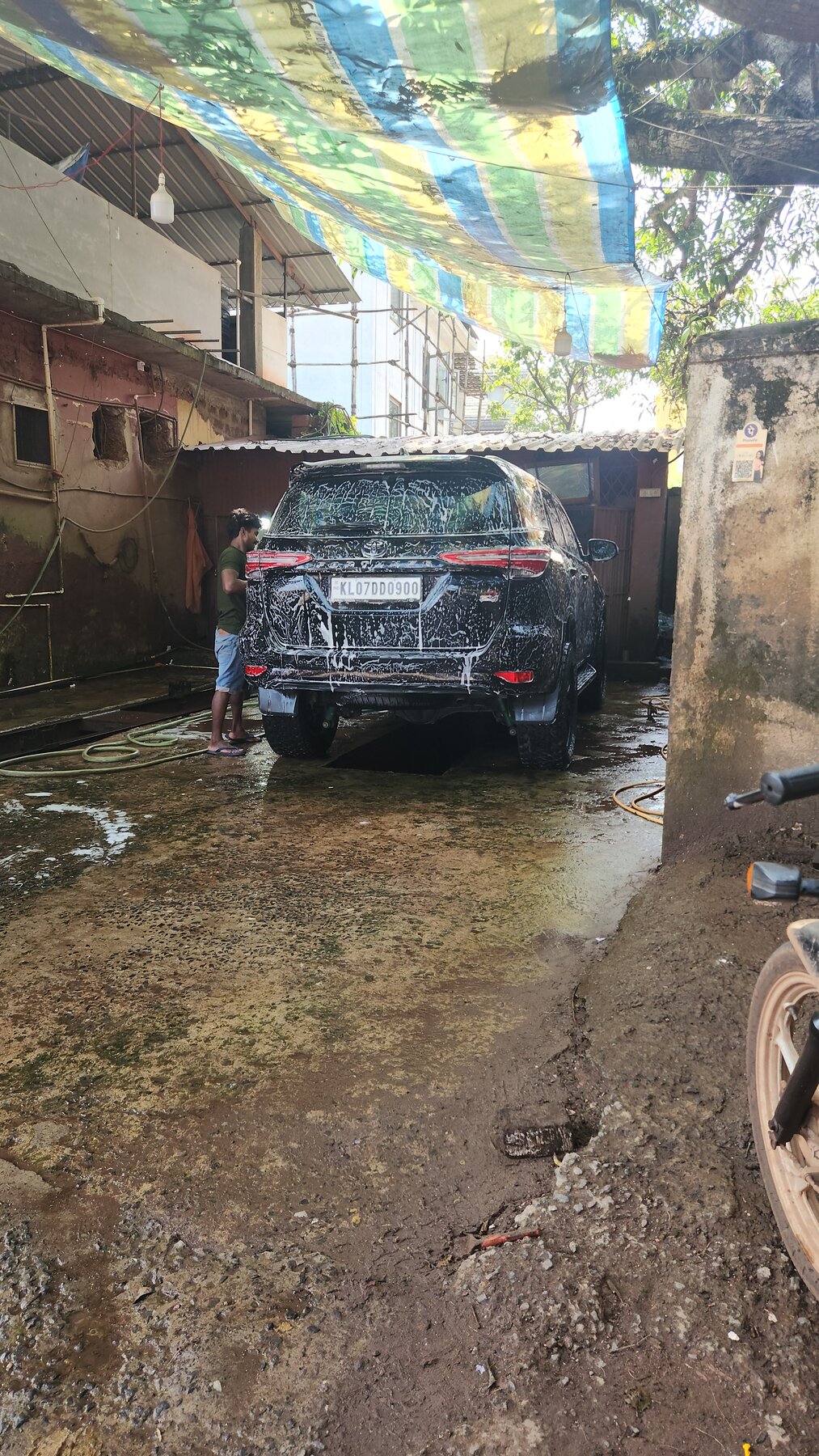 The Fortuner being washed at a small roadside car wash in Vagator under a striped tarp