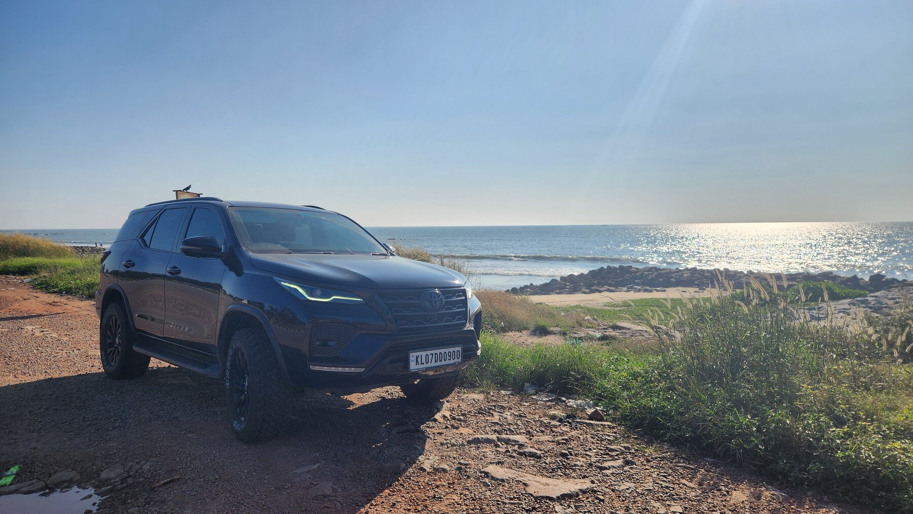 The Toyota Fortuner parked at a coastal pullout on NH66 with the Arabian Sea sparkling in the afternoon sun