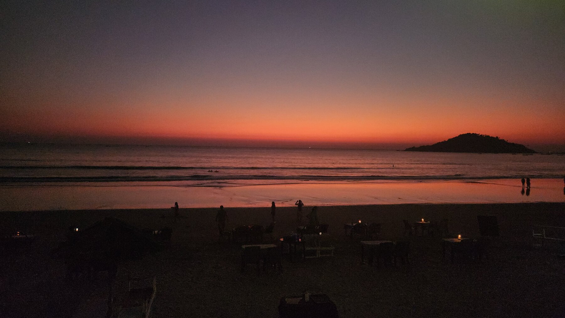 Sunset on Palolem beach with the small island silhouette and candle-lit shack tables in the foreground