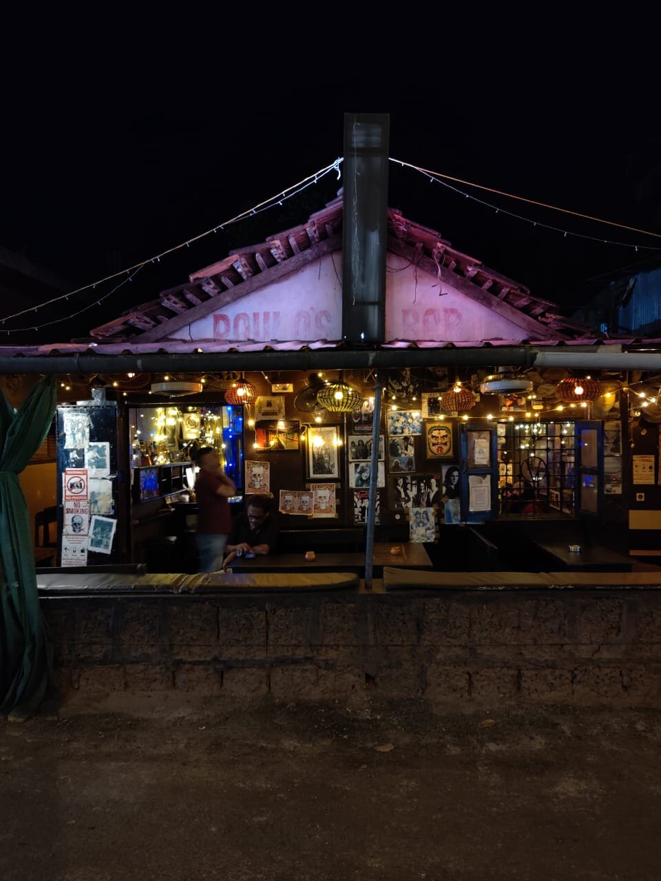 The exterior of Paulo's Bar in Vagator at night with fairy lights and band posters covering the walls