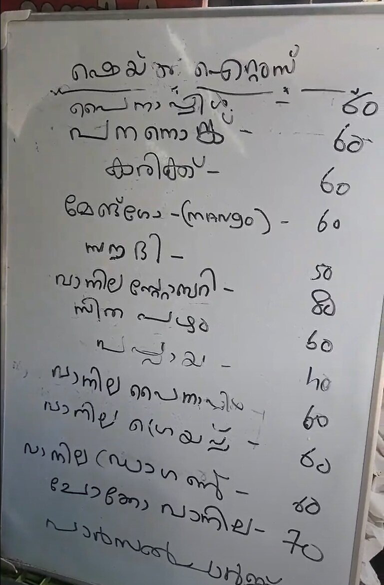 The handwritten Malayalam menu of shakes on a whiteboard at Thomson Fruits